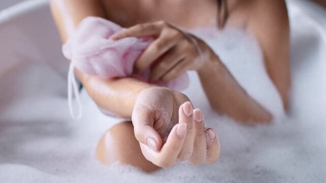 A young Asian woman enjoys a pampering bath experience at home, focusing on skin and body care. The relaxing atmosphere highlights self-care practices in a cozy bathroom setting.
