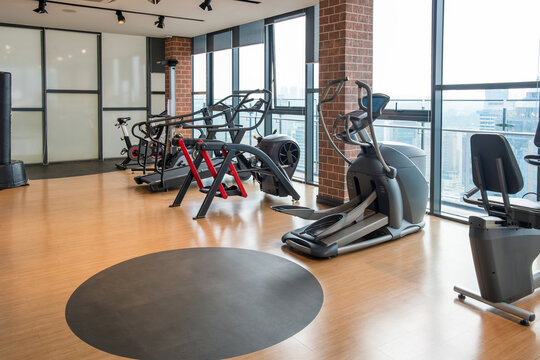 Modern gym interior with various fitness machines including elliptical trainers, treadmills and bikes and large windows with panoramic city view. Urban wellness, fitness, luxury, contemporary living