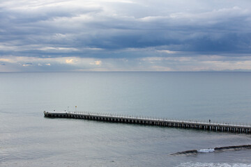 Fototapeta premium Gentle sunbeams pierce through a blanket of clouds, illuminating the calm sea and misty coastal mountains. The soft light creates a serene and ethereal atmosphere, highlighting the peaceful beauty