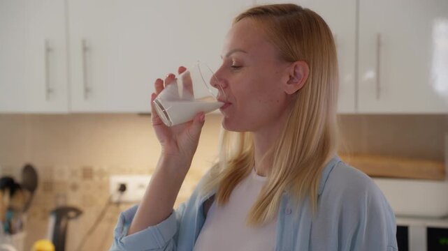Youthful caucasian woman smiling in kitchen while enjoy cool glass of milk, promoting healthy morning routine rich in calcium and wholesome dairy nutrition