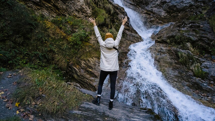 Obraz premium Woman celebrating joyfully at a scenic waterfall in a lush forest during a sunny afternoon near a hiking trail