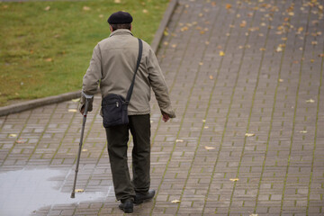 An old man with an orthopedic cane walks alone along a gloomy street
