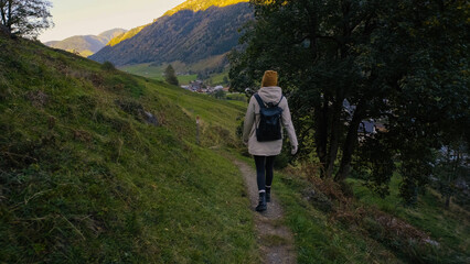 Obraz premium Hiking along a winding path in the mountains during golden hour, surrounded by lush greenery and scenic views of a quaint village