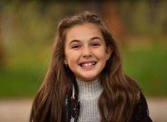 Fototapeta premium Portrait of a happy child girl outside, looking at the camera and smiling.