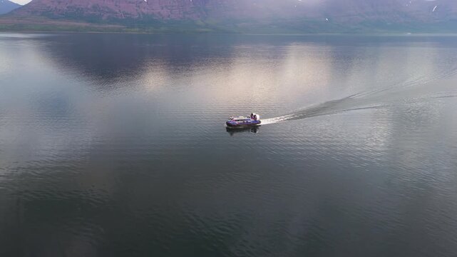 Aerial view captures hovercraft gliding across calm water at sunset with long wake. Mountain, reflection and soft cloud add scale. Putorana Plateau, Lake Lama, Siberia, wild region for tourism