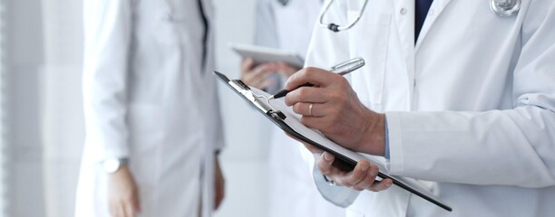 Doctor writing on a clipboard during a medical team discussion, collaborating on patient care, documentation, and healthcare strategy in a clinical setting