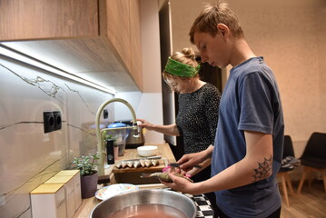 Teen boy and woman preparing fish together in a cozy home kitchen, cleaning fresh catch over the sink under warm light — family cooking, domestic lifestyle and teamwork concept