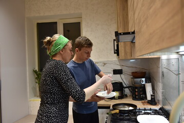 Woman and teenage boy cooking together in a cozy home kitchen, preparing food over the stove under warm evening light — family time, teamwork, and everyday life concept