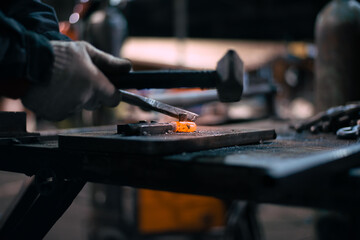 In the blacksmith's workshop, the blacksmith is leveling the red-hot metal with a hammer. A red-hot piece of metal with scale is being prepared for hardening. High quality photo
