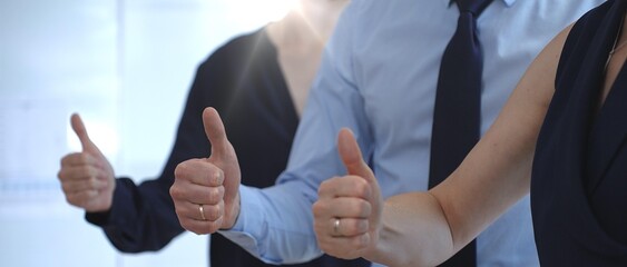 Business people team showing thumbs up gestures in a row, expressing approval, agreement, success, and full support for a project or strategy in a corporate office setting with sun flair