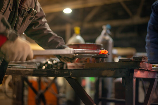 In the blacksmith's workshop, the blacksmith is leveling the red-hot metal with a hammer. A red-hot piece of metal with scale is being prepared for hardening. High quality photo