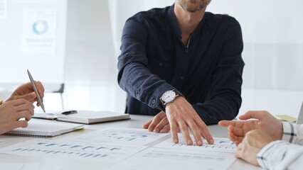 Professional colleagues reviewing financial charts, collaborating on strategic planning, gesturing toward data visualizations during corporate meeting in contemporary workspace