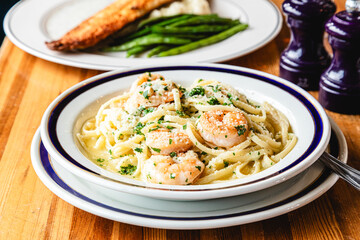 Pasta with shrimp and a white sauce in a brightly lit restaurant with other dishes in the background 