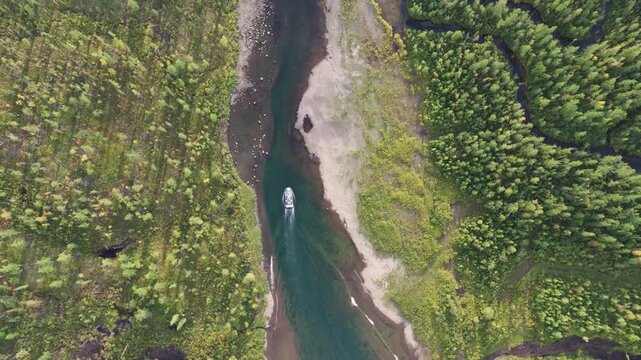 Aerial view of a tight river corridor winding through bright green tundra as a boat keeps centerline, leaving a wake along shallow banks. Subtle tilt reveals sand pockets, stones and crisp water aroun