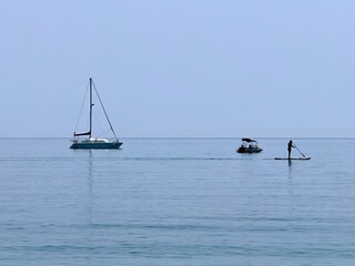 sailboat, small touristic boat and stand up paddle board on the ocean with flat waves, holiday, vacation, tourism, sport