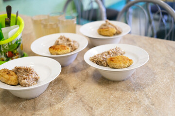 School cafeteria meal featuring bowls of oatmeal and baked goods on a table, with a colorful container and glasses in the background, showcasing nutritious food options for students