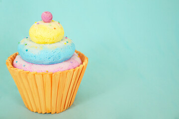 Artificial foam candy cupcake with vibrant colors on a turquoise background, featuring playful textures and ample copy space for creative design elements