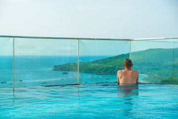 Man relaxing in rooftop infinity pool with stunning panoramic view of tropical island and...