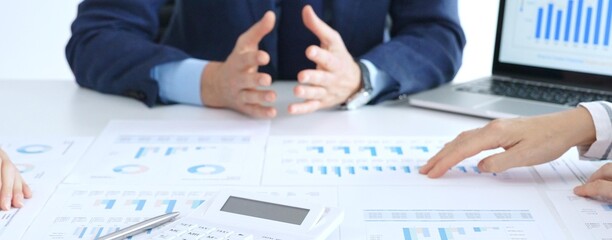 Business people reviewing financial charts and reports in office, using a laptop and calculator while engaging in discussions about strategy and performance