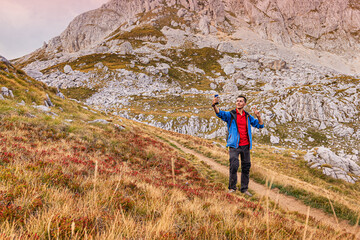 Fototapeta premium Hiker man taking selfie on mountain trail, showing peace sign, embracing nature and outdoor adventure