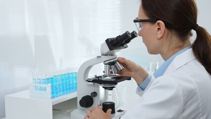 Female scientist examining microscope slide, analyzing chemical sample in sterile laboratory environment, performing precision medical research. Medicine and science concept