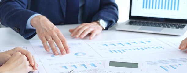 Business professionals collaborating at a conference table, reviewing financial charts and reports, using a laptop and calculator while engaging in discussions about strategy and performance