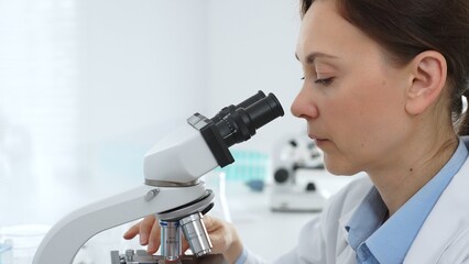 Female scientist examining samples through a microscope in a modern lab, conducting pharmaceutical research and developing treatments. Medicine, healthcare and science concept