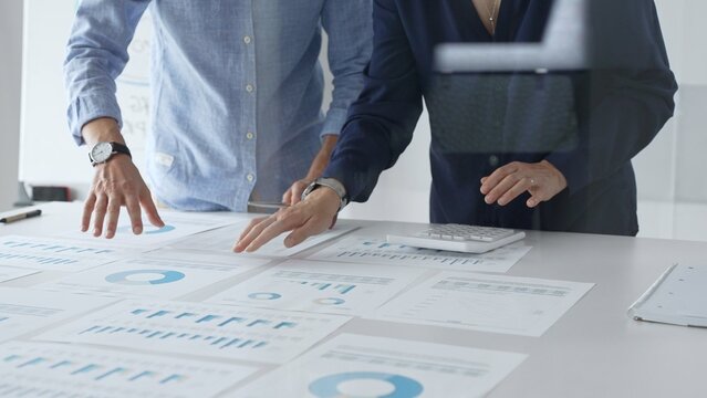 Professional team collaborating, reviewing financial graphs, calculating metrics, discussing performance insights and strategic planning in modern corporate workspace. Business people concept - Powered by Adobe