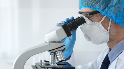Male scientist wearing protective gear examining microscope slide, analyzing research sample in sterile laboratory environment. Health care and science concept