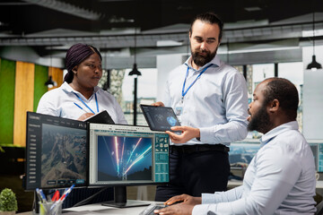 Team of sustainable energy tech company technicians monitoring eco power line towers. Teamworking colleagues use CAD software on PC to upgrade transmission tower systems, reducing carbon emissions © DC Studio