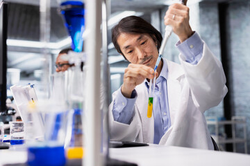 Senior molecular biologist conducting pipetting operation for sample preparation in controlled laboratory environment. Asian research facility professional using pipette for liquid measurement