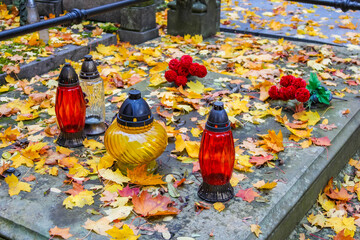 Red glass memorial candles placed among colorful autumn leaves on grave covers at Powązki Cemetery...
