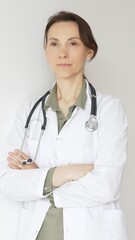 Fototapeta premium Female medical professional in white lab coat, stethoscope draped, standing with crossed arms and displaying confident, authoritative healthcare demeanor. Medicine and health care