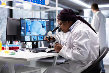 Black scientist examining samples under microscope in a modern laboratory. Research work integrates...