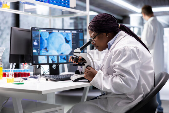 Black scientist examining samples under microscope in a modern laboratory. Research work integrates biotechnology, molecular science and advanced diagnostics to shape medical discovery.