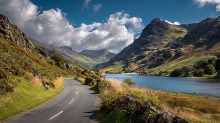 Majestic mountain valley unfolds with a winding road leading to a serene blue lake under dramatic clouds creating a breathtaking natural landscape.
