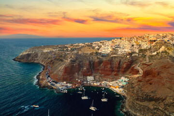 Aerial drone view of famous Oia village with white houses, blue dome churches and Old port Amoudi bay during colorful sunset on Santorini island, Aegean sea, Greece
