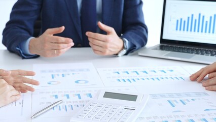 Business professionals collaborating at a conference table, reviewing financial charts and reports, using a laptop and calculator while engaging in discussions about strategy and performance