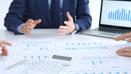 Business professionals collaborating at a conference table, reviewing financial charts and reports, using a laptop and calculator while engaging in discussions about strategy and performance