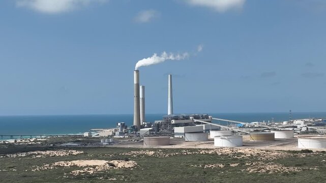 Industrial chimneys of EAPC (Eilat Ashkelon Pipeline Company) near Ashkelon, Israel. Power and energy infrastructure with blue sky and urban background.