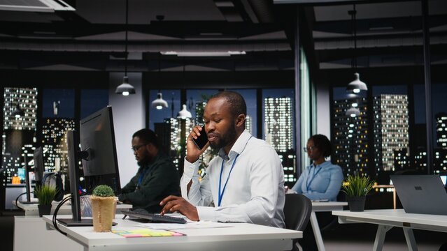 African american consultant makes important phone call after hours, contacting senior consultant to share business growth ideas and investment opportunities on a secure telephone line. - Powered by Adobe