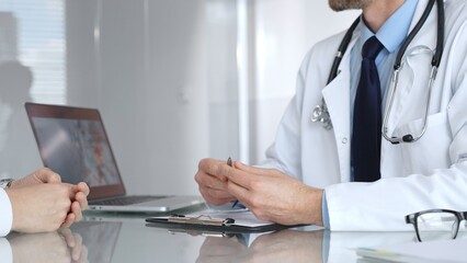 Doctor consulting patient about healthcare, discussing medical examination results on laptop in clinic office. Medicine, healthcare and science concept