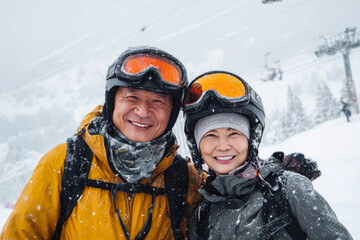 A happy Asian married couple in ski masks and gear hugging in the snowy mountains. Concept of a family trip to a ski resort, happy moment