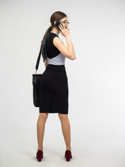 Fototapeta premium Businesswoman talking on phone. Young woman dressed as entrepreneur. Woman manager with briefcase over shoulder. Businesslady in business attire and skirt. Businesswoman standing on light background