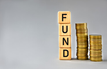 FUND - word on wooden cubes on the background of stacks of coins