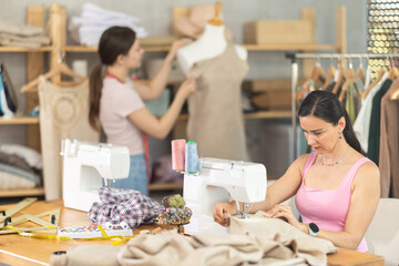 Friendly middle-aged woman tailor using sewing machine at workshop
