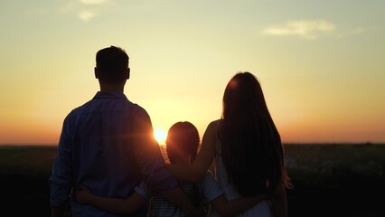 Family outdoors, parents little daughter. Family hugging outdoors, sunset. Family, mother father girl hug child, silhouette. Caring parents. Happy dad mom little daughter hugging in park, close-up
