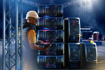 Sound engineer with laptop configures large speaker system, optimizing audio setup and acoustic quality for concert event production.