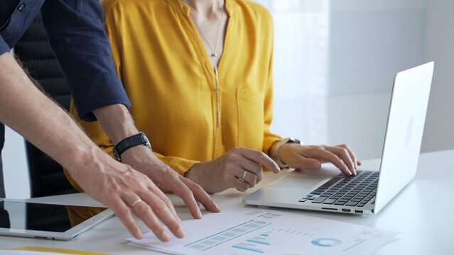Business colleagues collaborating on a project while analyzing financial charts and entering data on a laptop in a modern office. Businesspeople concept