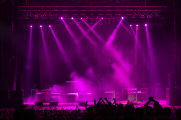 Stage lighting show with purple spotlights and smoke effects as audience cheers before live music performance. Event production, concert preparation, entertainment industry.